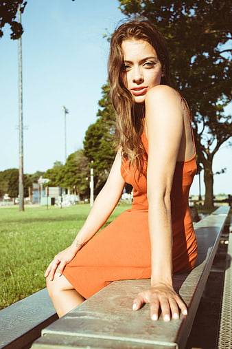Brunette Woman in Orange Dress Sitting on Park Bench