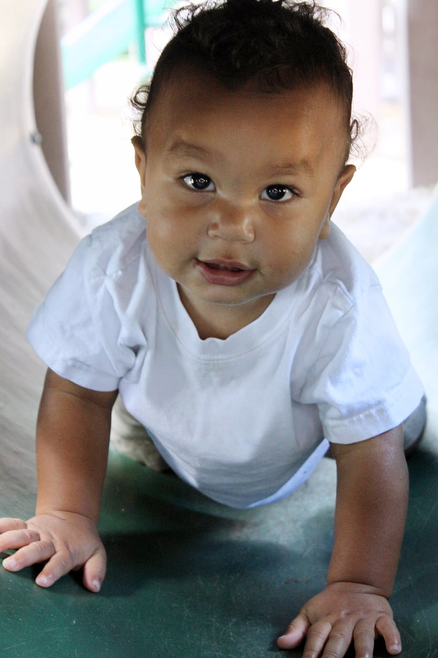 Cute baby crawling on green surface looking at camera
