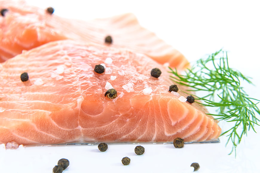 Fresh raw salmon fillet with dill, salt, and pepper on white background