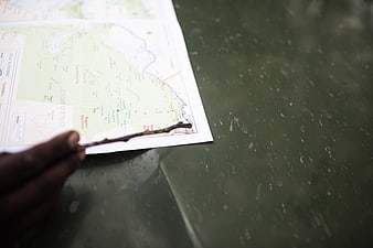 Hand Using Stick to Point at Map on Green Table