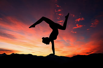 Woman performing yoga handstand silhouette against vibrant sunset sky