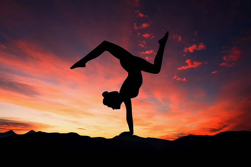 Woman performing yoga handstand silhouette against vibrant sunset sky