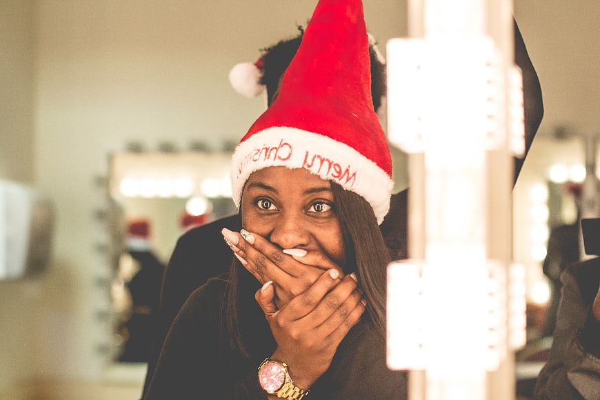 Surprised Black Woman in Santa Hat Looking in Mirror