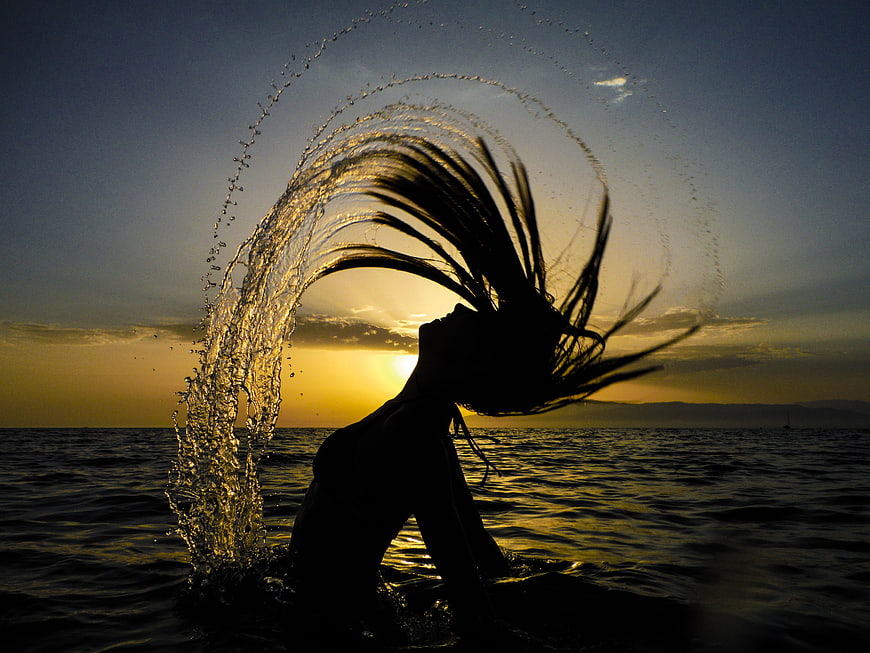 Silhouette of woman shaking wet hair in ocean at sunset