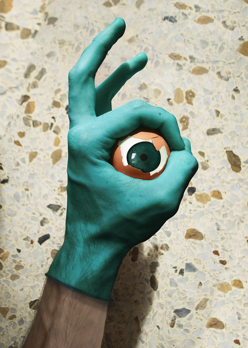 Teal painted hand holding cracked egg with eye inside