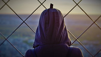 Person in Hoodie Looking Through Chain Link Fence at Dusk