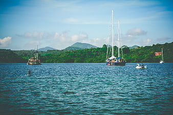 Sailboat and jet ski on calm tropical waters with green hills
