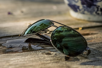 Aviator sunglasses on wet wooden table with reflection