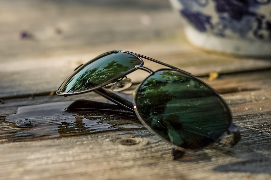 Aviator sunglasses on wet wooden table with reflection