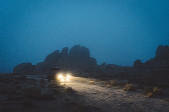 Off-road SUV with headlights in desert landscape at night