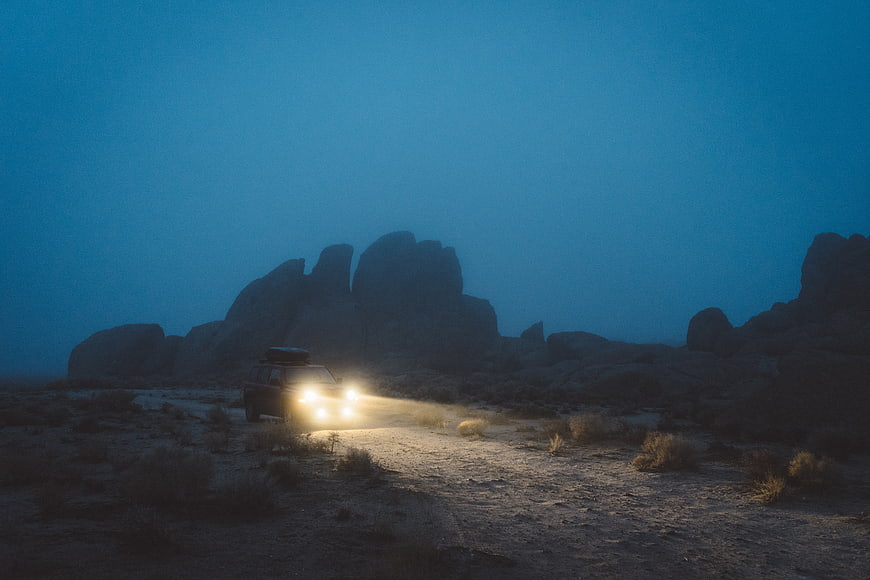 Off-road SUV with headlights in desert landscape at night