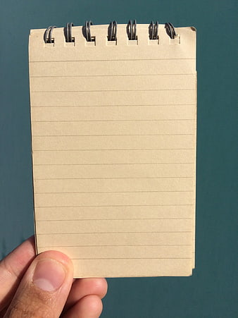 Hand holding blank spiral notepad against teal background