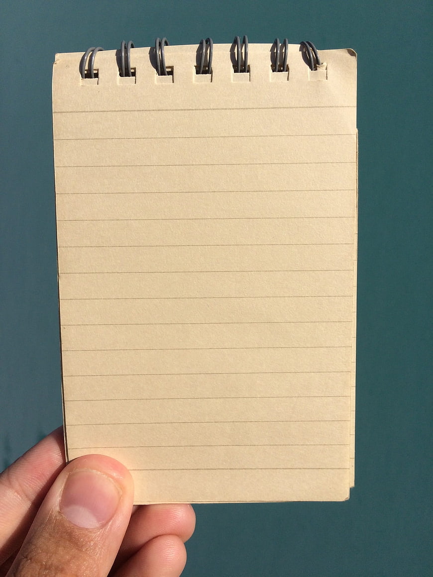 Hand holding blank spiral notepad against teal background