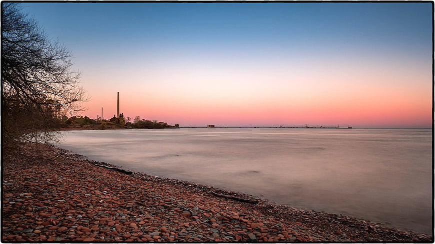 Serene Pebble Beach at Sunset with Industrial Skyline
