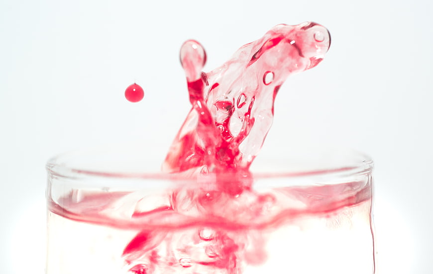 Red liquid splash in glass with white background