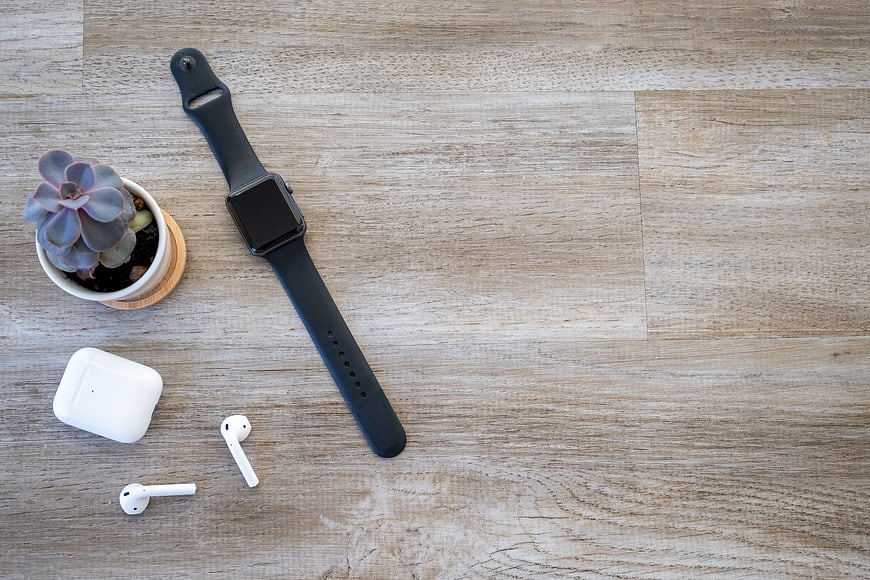 Flat lay of smartwatch, wireless earbuds, and succulent on wood