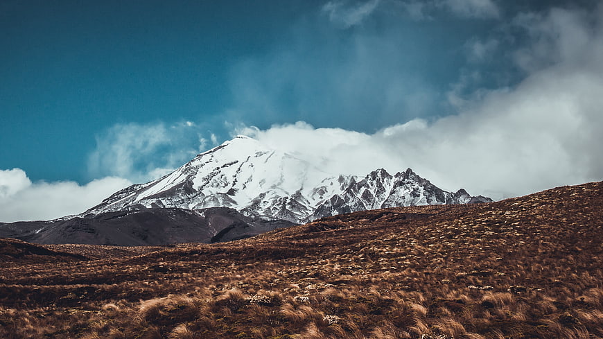 Snow-Capped Mountain Peak with Clouds and Brown Grassland
