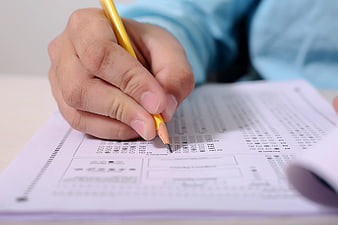 Close-up of hand filling out standardized test answer sheet with yellow pencil
