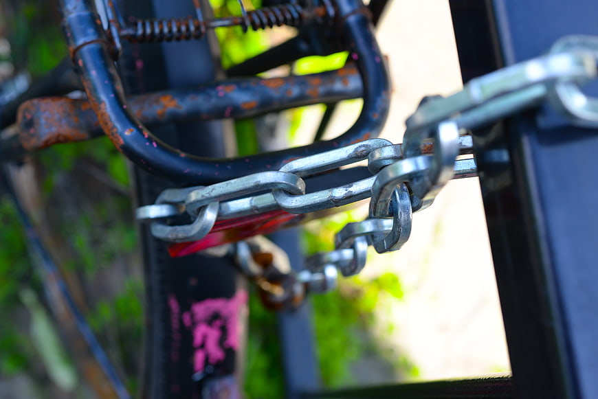 Close-up of rusty bicycle secured with heavy metal chain lock
