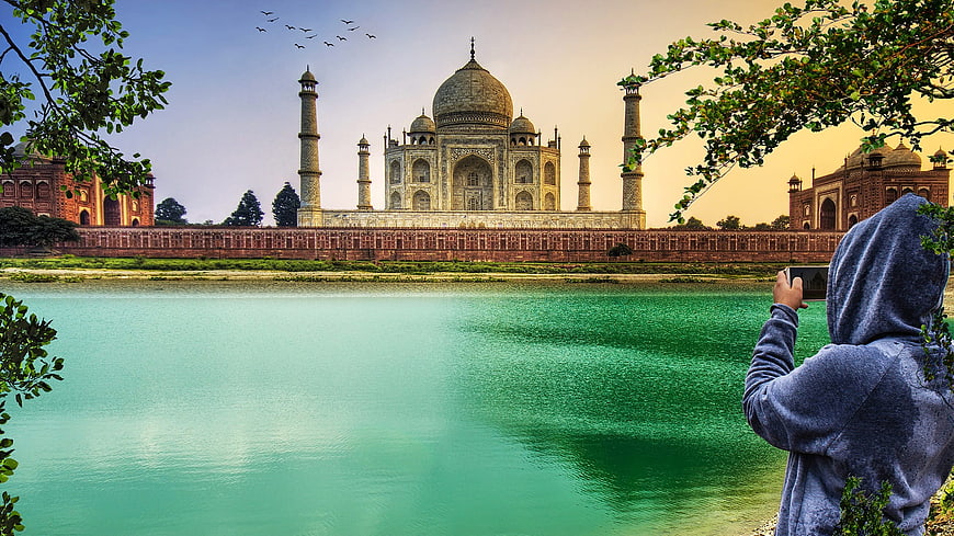 Tourist photographing Taj Mahal from riverbank at sunset