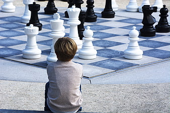 Young boy sitting and thinking at giant outdoor chessboard