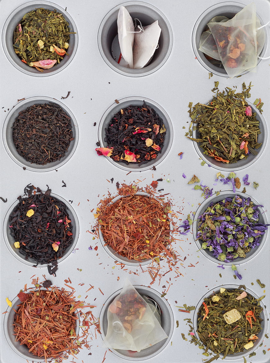Flat lay of various loose leaf teas and tea bags in metal cups