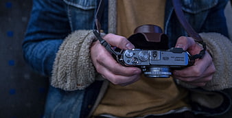 Close-up of hands holding a silver Fujifilm X100 camera