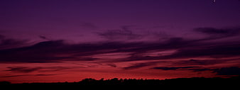 Dramatic purple and red sunset sky with silhouette landscape