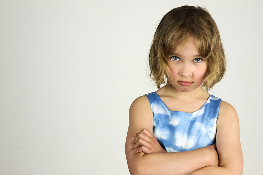 Angry little girl with crossed arms on white background