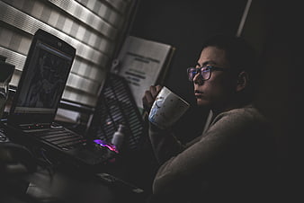 Man drinking coffee while working on laptop at night