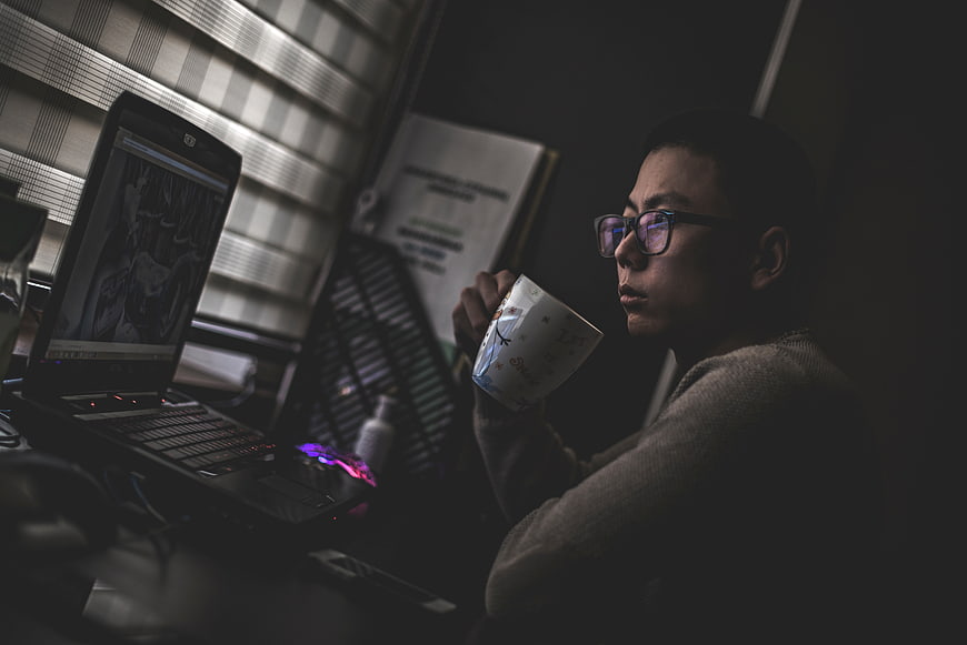 Man drinking coffee while working on laptop at night