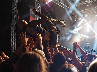 Concert crowd surfing with dramatic stage lighting and energetic atmosphere