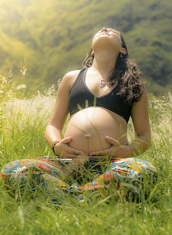 Pregnant woman meditating in a sunny green meadow