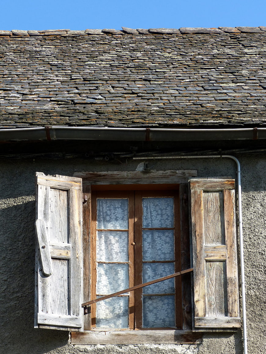 Rustic stone roof and weathered wooden window with shutters