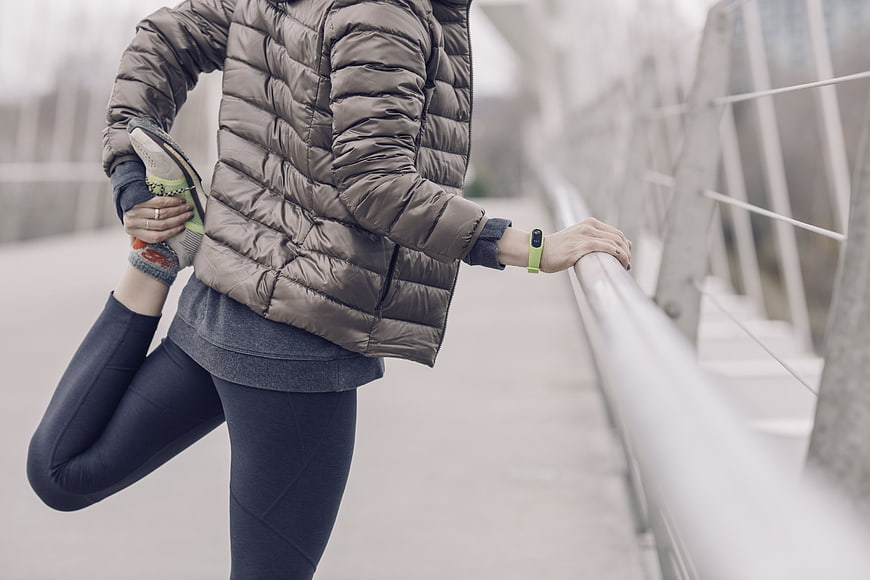 Woman stretching leg in puffer jacket on bridge