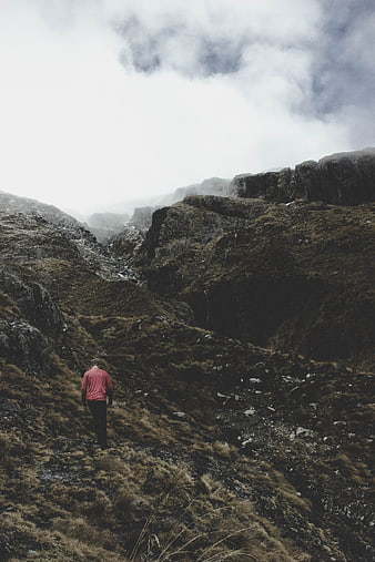 Hiker walking on rugged mountain trail in misty highlands