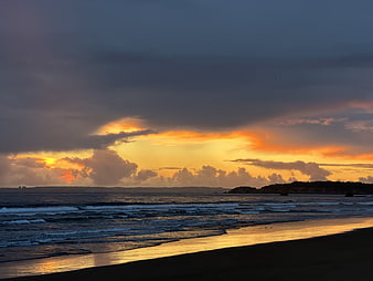 Dramatic sunset over ocean waves with golden light reflecting on wet sand