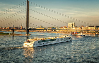 White cruise ship sailing under cable-stayed bridge at sunset