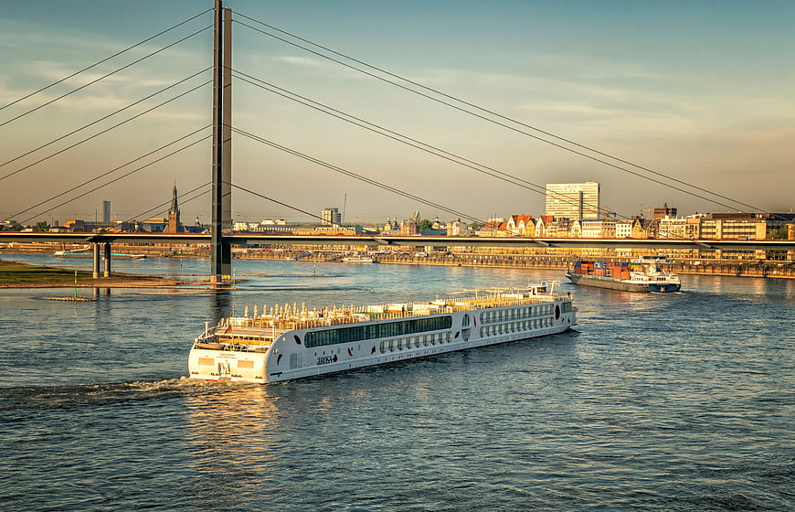 White cruise ship sailing under cable-stayed bridge at sunset