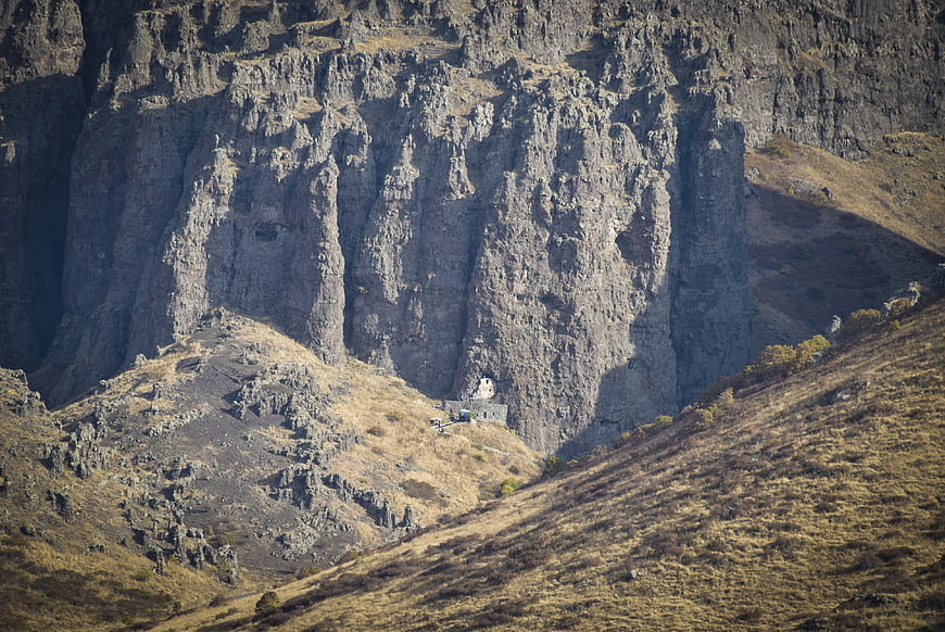 Small white building nestled at the base of a massive rocky cliff