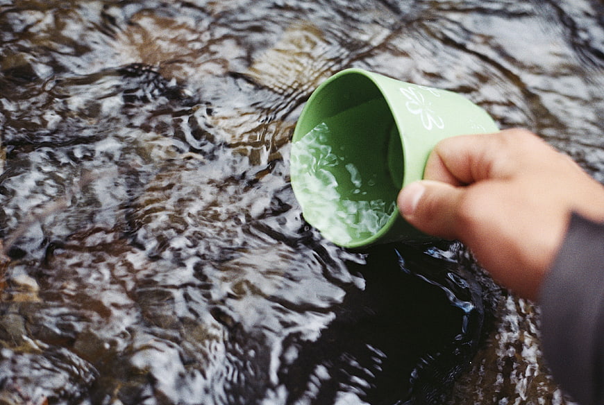 Hand filling green cup with water from flowing stream