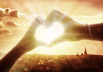 Hands forming heart shape framing sunset over European city skyline