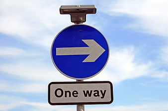 Blue One Way Traffic Sign with Arrow Against Sky