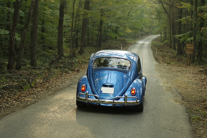 Vintage Blue Volkswagen Beetle Driving on Forest Road