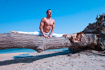 Muscular Man Doing Splits on Driftwood Log at Beach