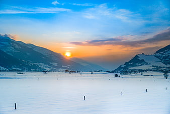 Sunset over snowy alpine valley with mountains and sky