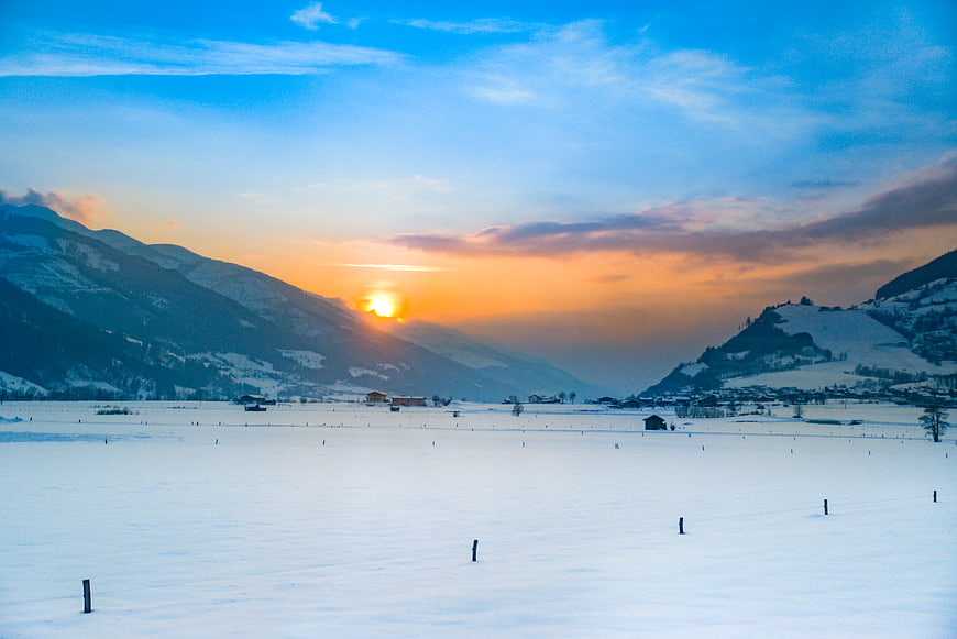 Sunset over snowy alpine valley with mountains and sky