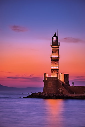 Illuminated Lighthouse at Sunset Over Calm Sea