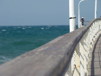 Close-up of weathered pier railing overlooking blue sea