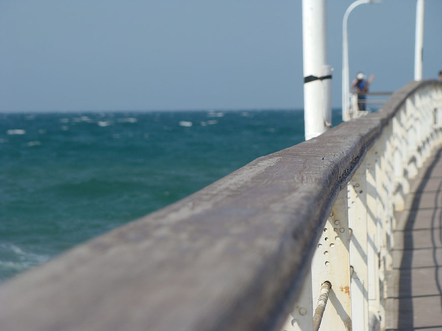 Close-up of weathered pier railing overlooking blue sea